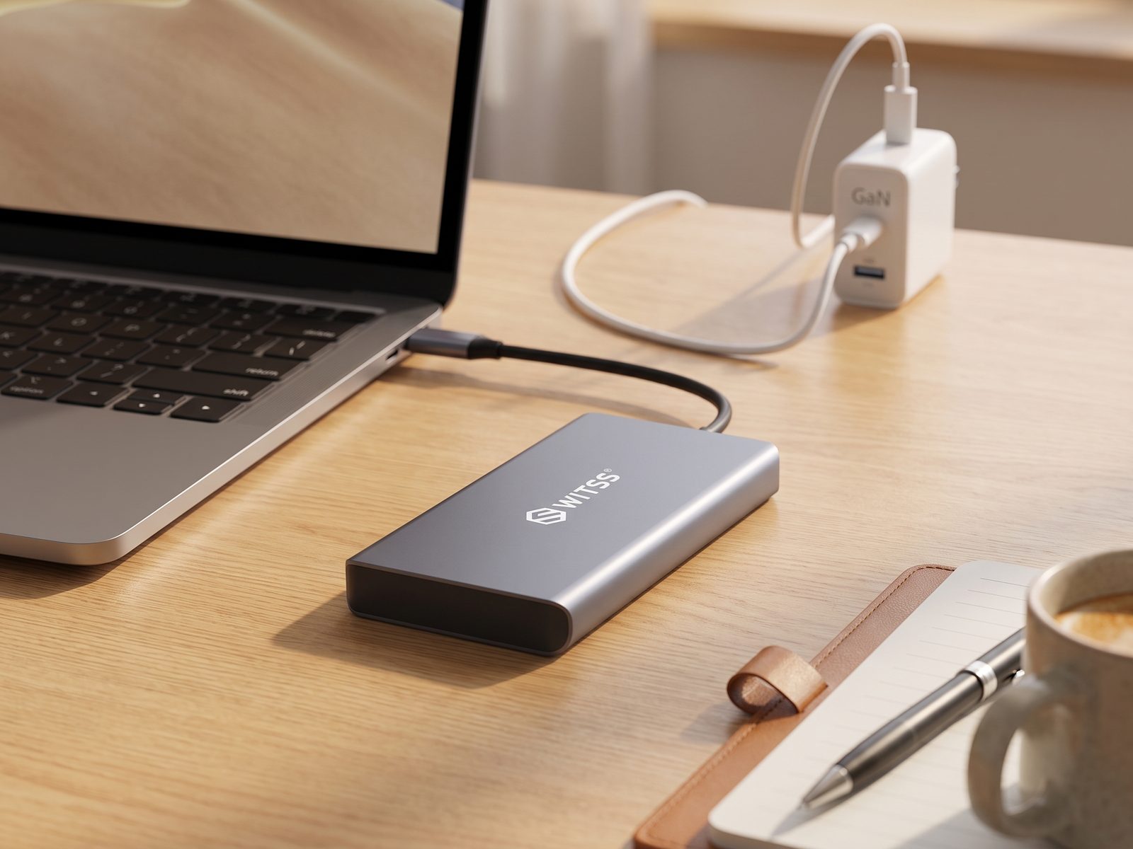 Switss® 12-in-1 hub op een bureau, laptop-oplaadkabel via een GaN-lader op de achtergrond