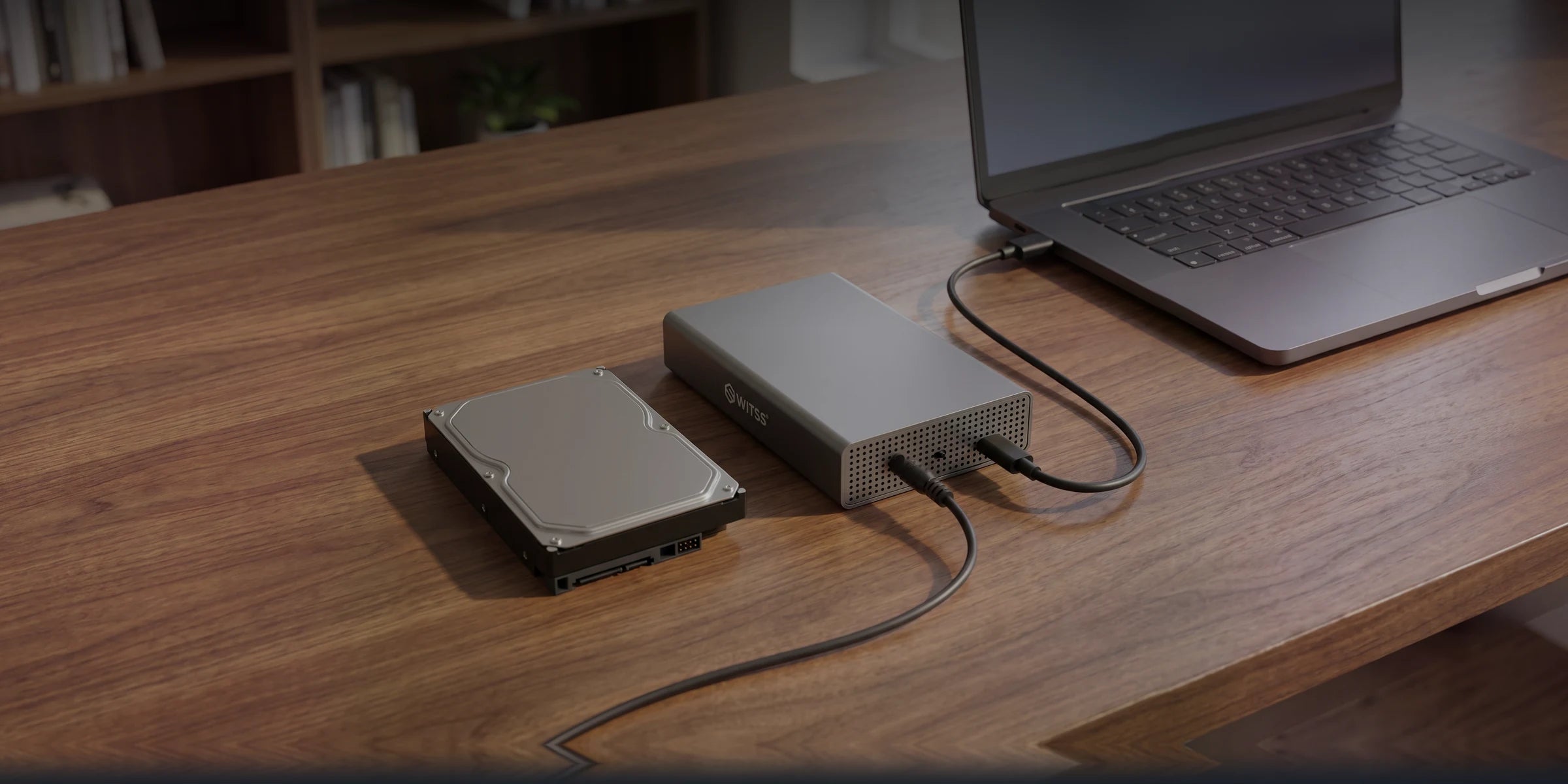Le boîtier Switss 3,5 pouces sur un bureau en bois à côté d'un disque dur nu, câble USB relié à un ordinateur portable et adaptateur secteur branché