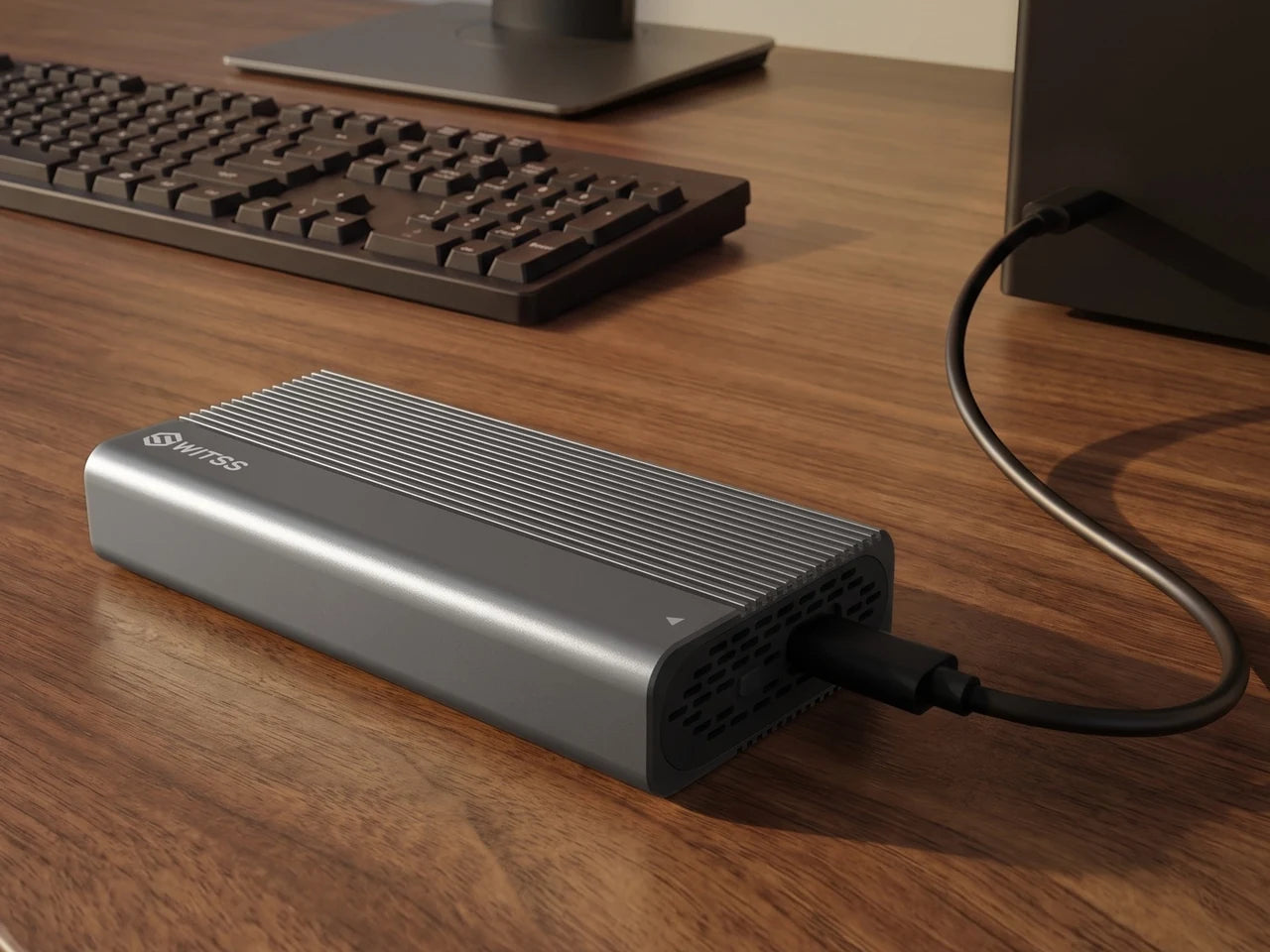 The Switss M.2 enclosure on a wooden desk, with the USB-C cable running to the USB port of a PC