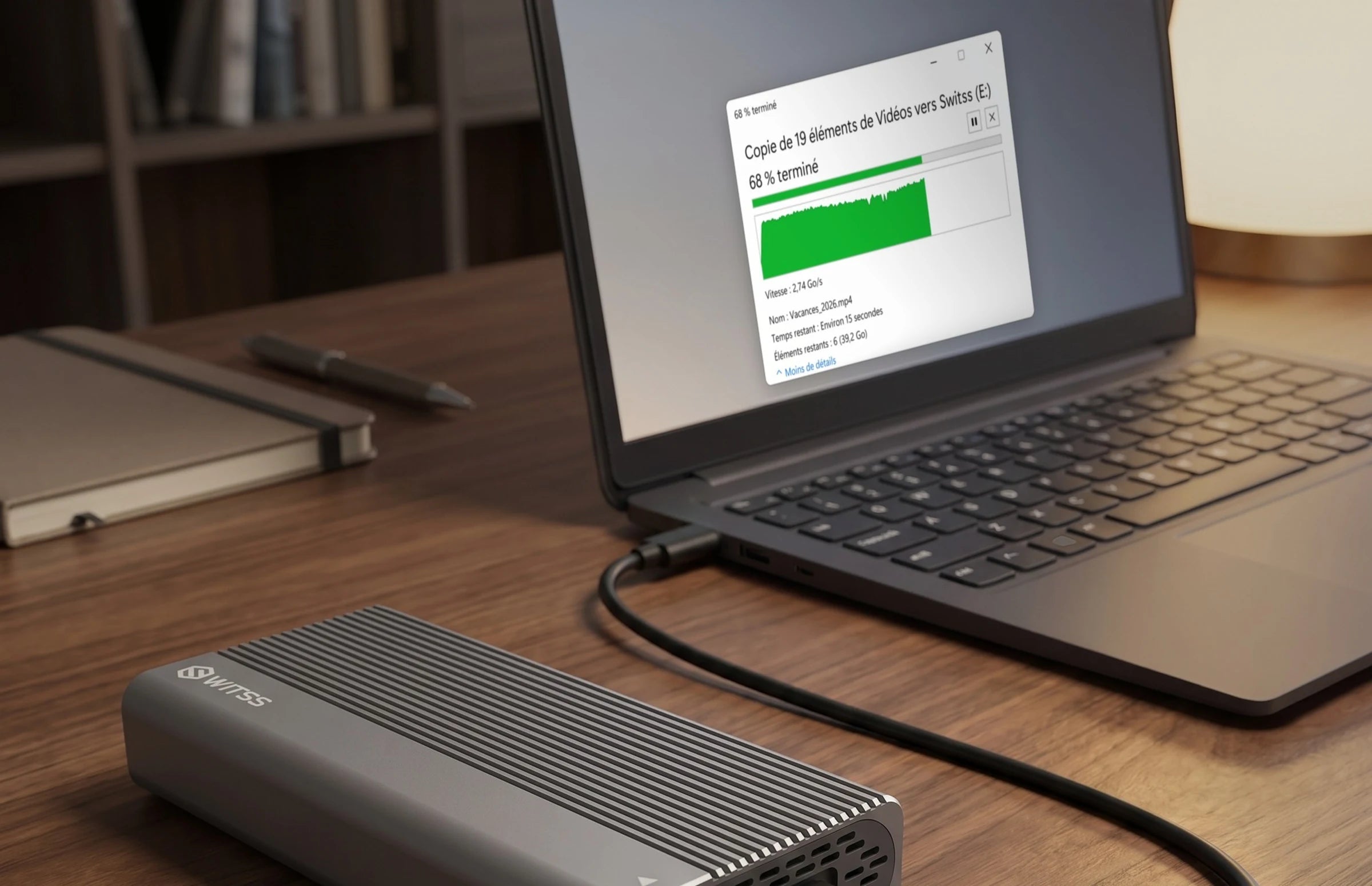 Le boîtier M.2 Switss relié à un ordinateur portable par le câble USB-C, avec une copie de fichiers vers le disque en cours à l’écran